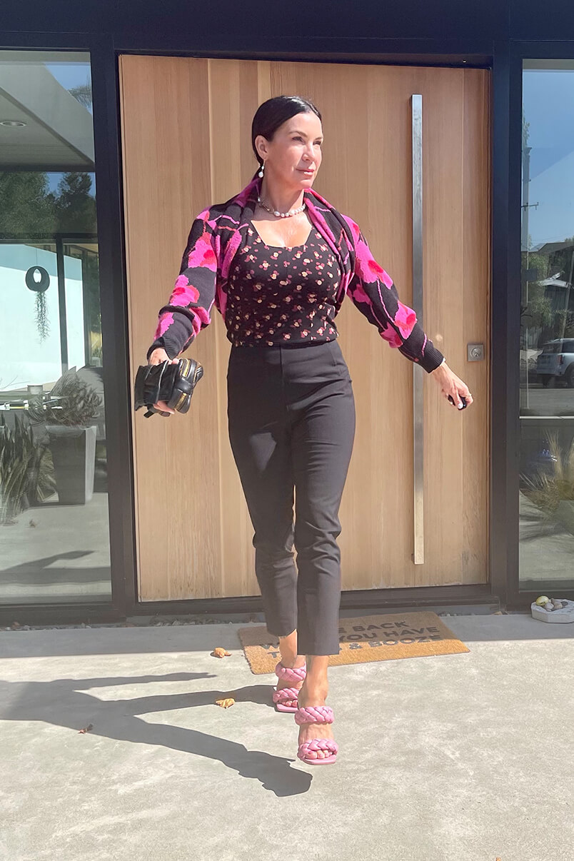 Kat Woodside, Chief Design Officer models her outfit of the day featuring the Lean Tank in Flower Burst, Rococo Pullover in Poppy Bloom, Dinner Trouser in Black and statement accessories.